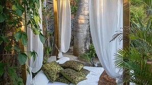 A wooden gazebo with a bed, white curtains, and green foliage. - Hotel Villa Morgane (Saint-Pierre)