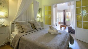 A bedroom with a canopy bed, a bedside table with a lamp, and a view of the outside through a large window. - Hotel Villa Morgane (Saint-Pierre)