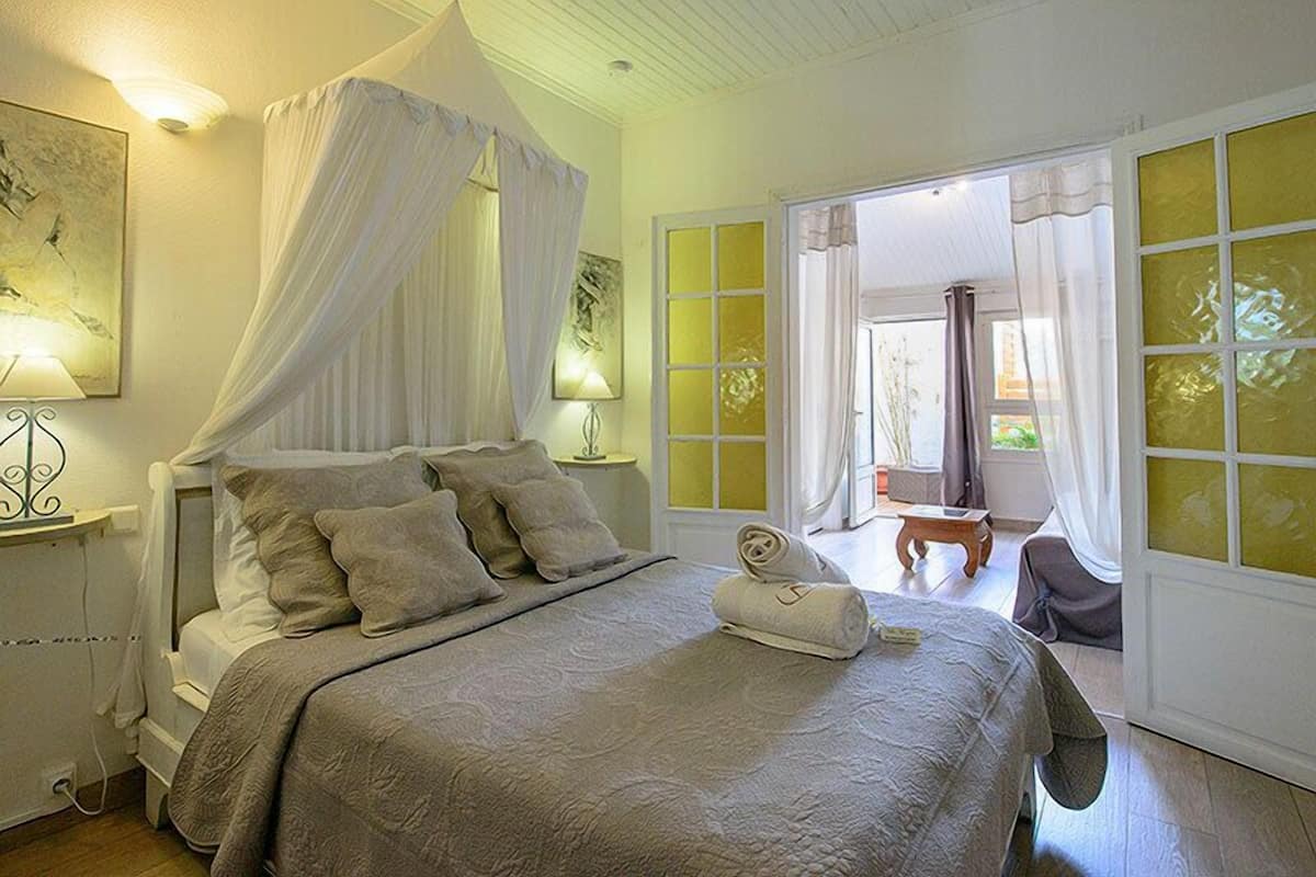 A bedroom with a canopy bed, a bedside table with a lamp, and a view of the outside through a large window.