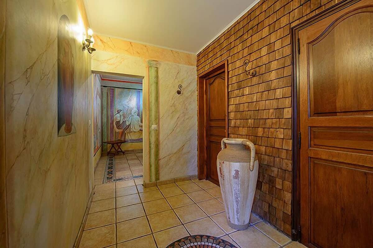 A hallway with marble walls, a tiled floor, a wooden door, and a large vase.