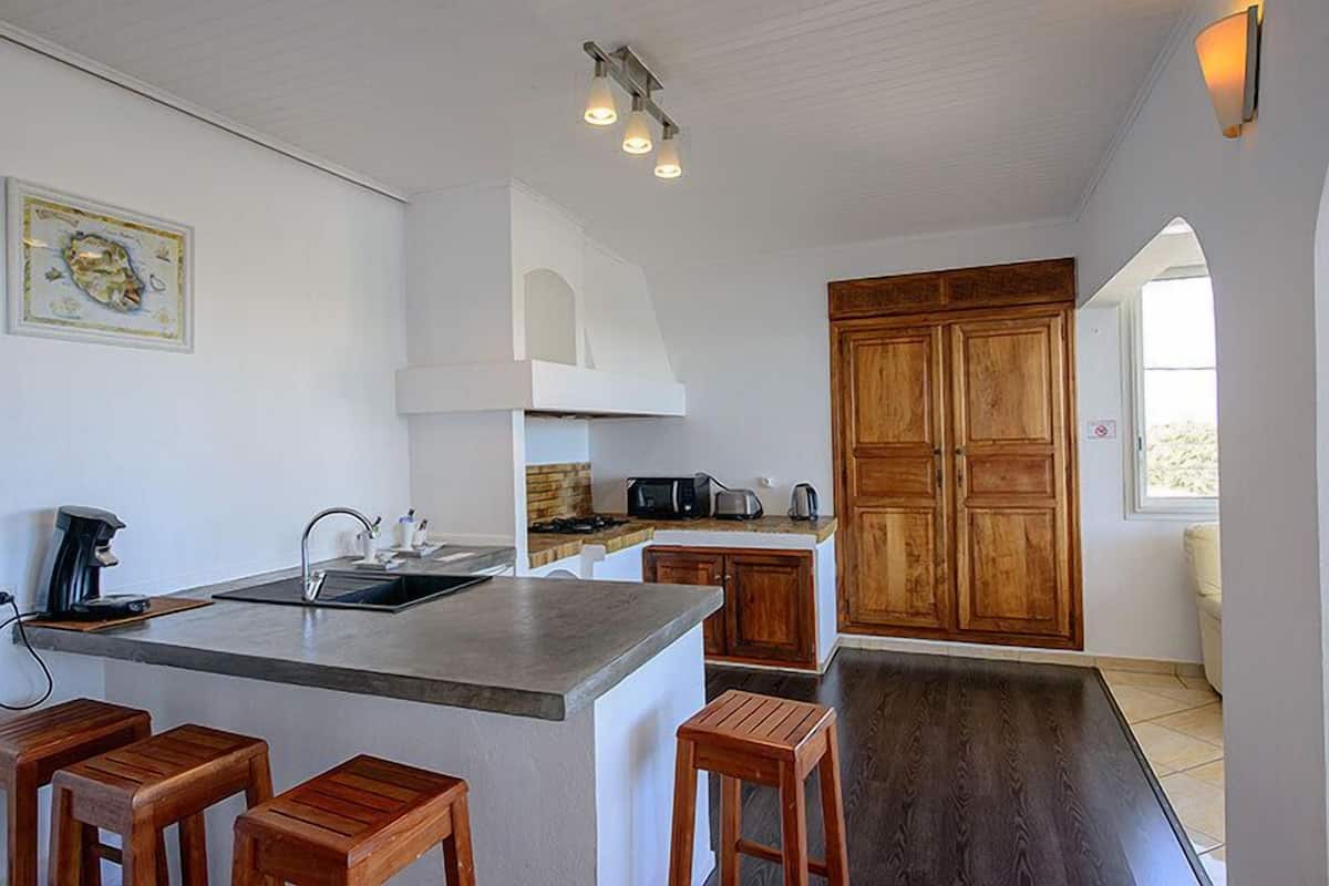 A modern kitchen with a central island, wooden stools, a built-in oven, and a large wooden cabinet.