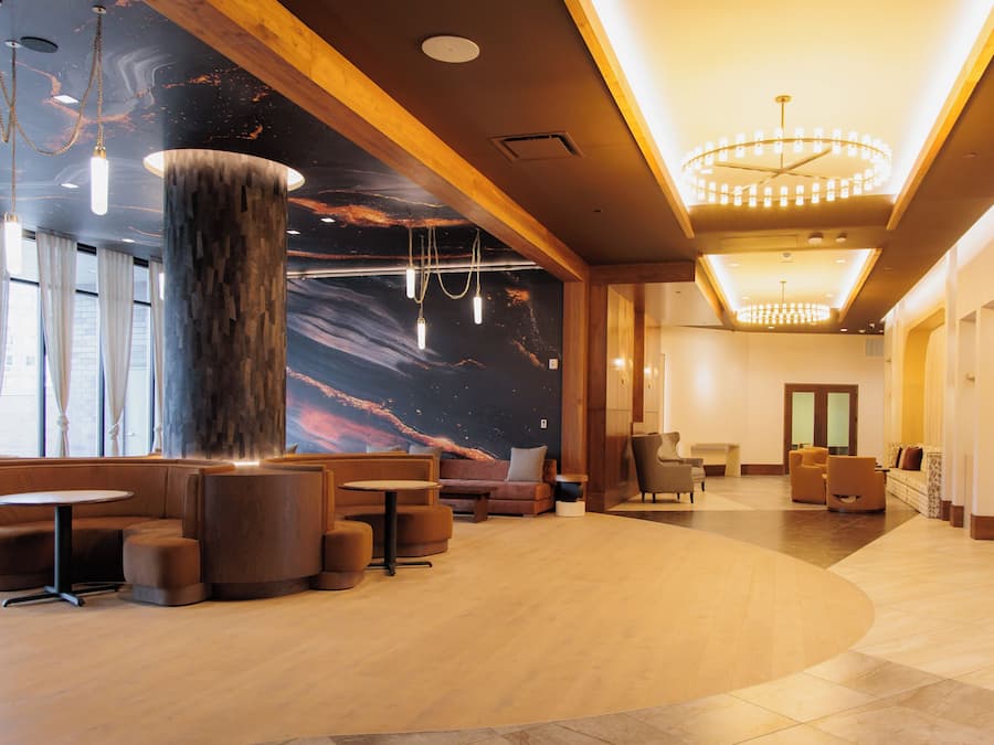 Een moderne lobby met een grote houten kolom, zithoeken en een muurschildering.