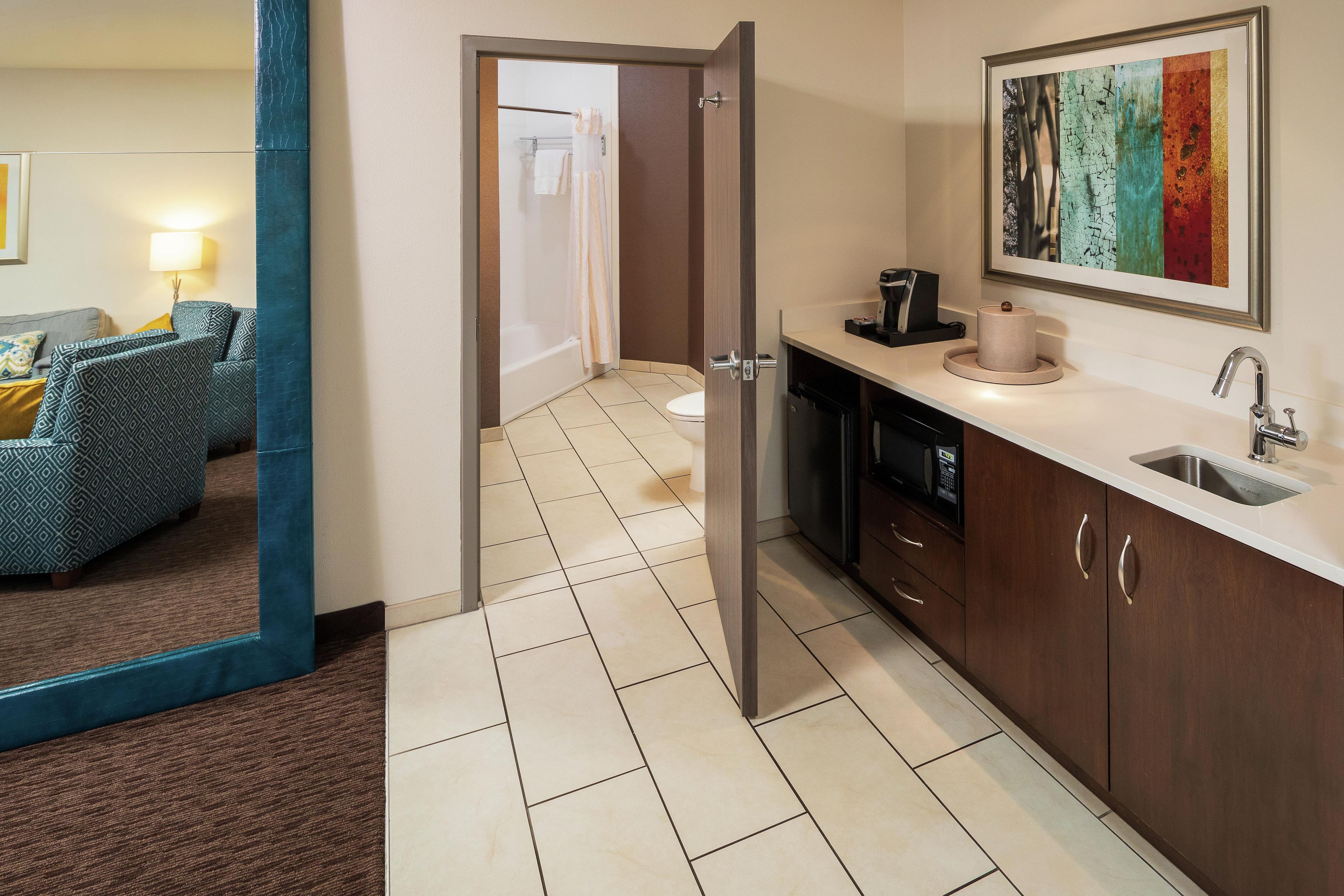 A hotel room with a kitchenette, a bathroom, and a living area.