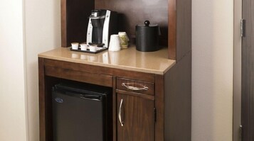 Una kitchenette compacta con cafetera, un refrigerador pequeño y un portavasos.
