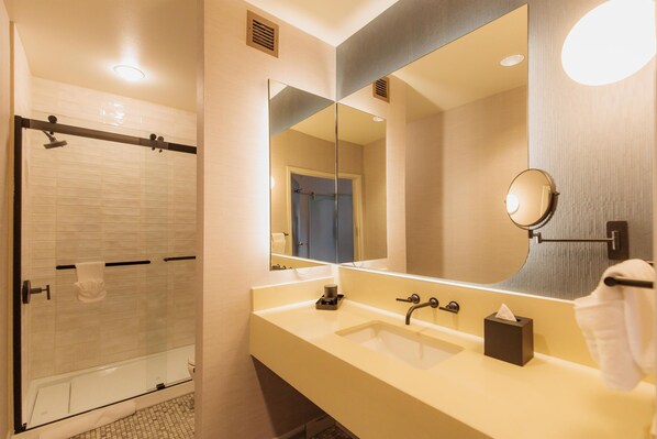 Un baño moderno con cabina de ducha de vidrio, un espejo grande y un mueble de tocador color beige con lavamanos.