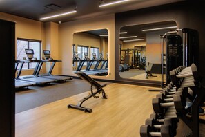 Une salle de sport équipée de tapis de course, d’un banc de développé couché et d’haltères.