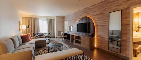 A modern hotel room with a living area, a dining table, and a TV.