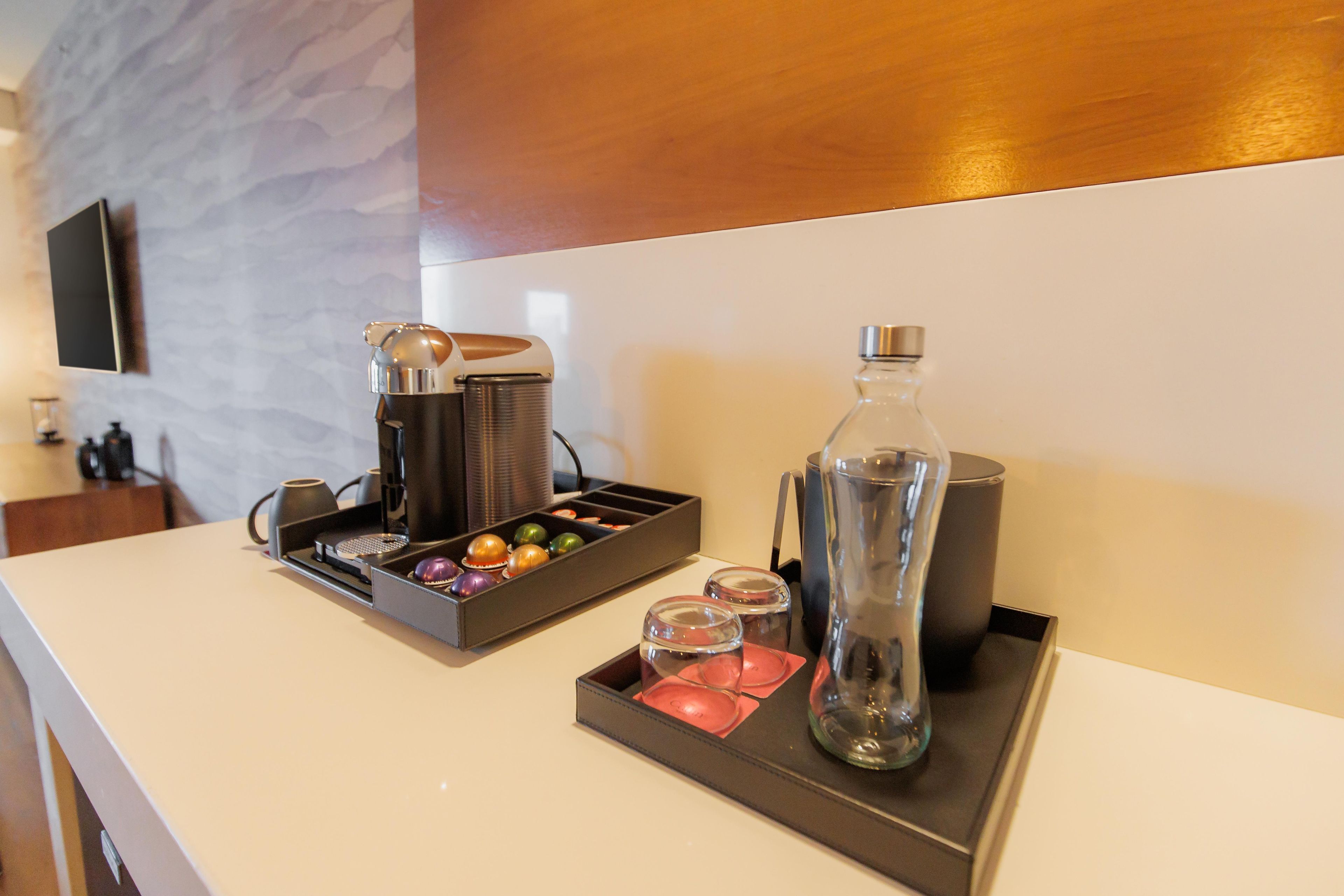 Mostrador de hotel con una cafetera, una botella de agua y una bandeja con vasos y un recipiente pequeño.