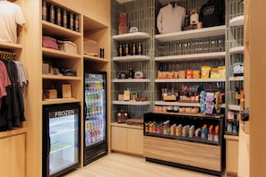 Un espacio comercial con estanterías llenas de diversos productos, un refrigerador exhibidor y una percha para ropa.