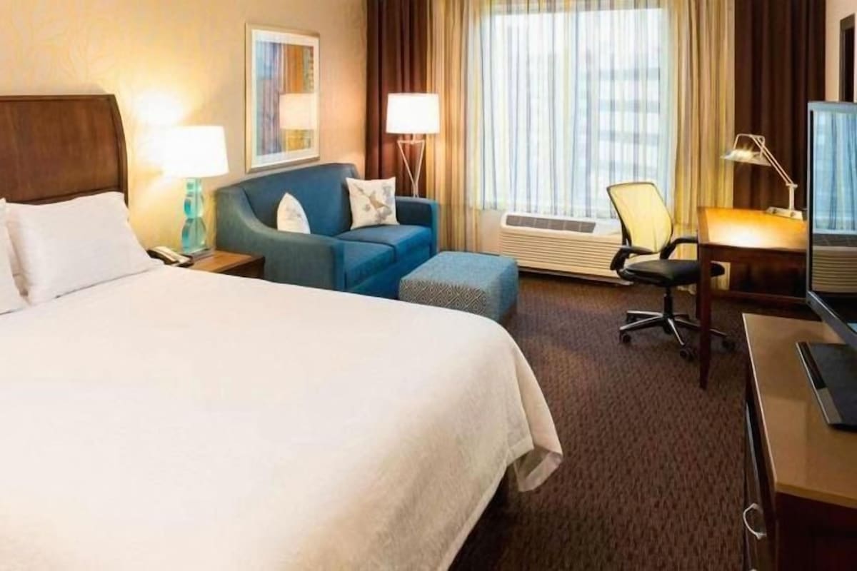 A hotel room with a large bed, a desk, a chair, and a sofa.