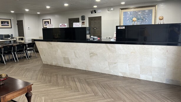 A reception area with a marble counter, a wooden herringbone floor, and a framed artwork above the counter. - Motel 6 New Boston, TX (New Boston)