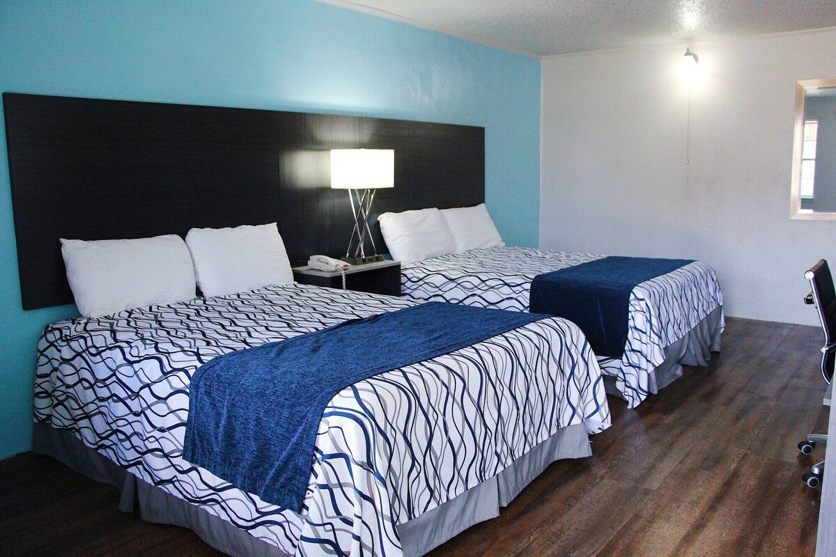A hotel room with two beds, a nightstand, a lamp, and a mirror.