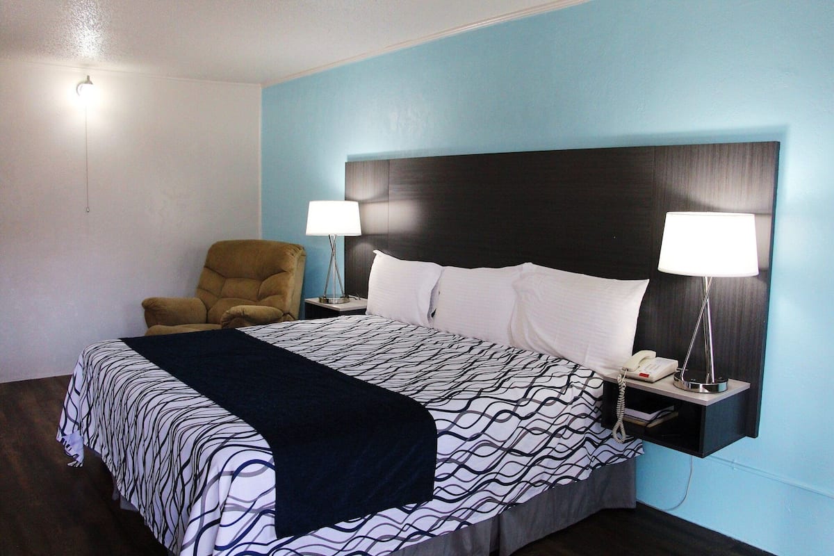 A hotel room with a bed, two bedside lamps, a chair, and a phone on the nightstand.