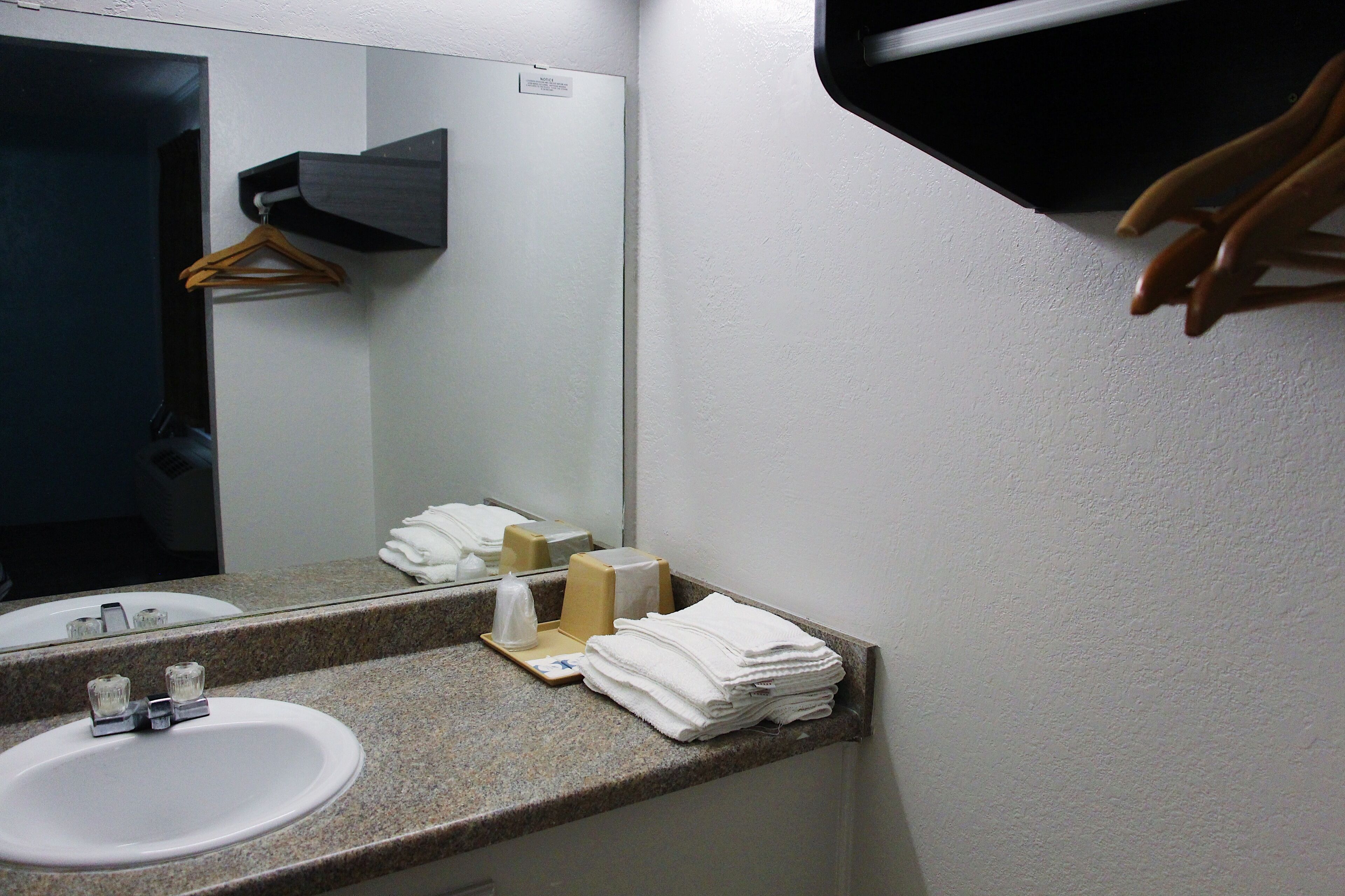 A bathroom with a sink, mirror, towel dispenser, and a hanging rack.