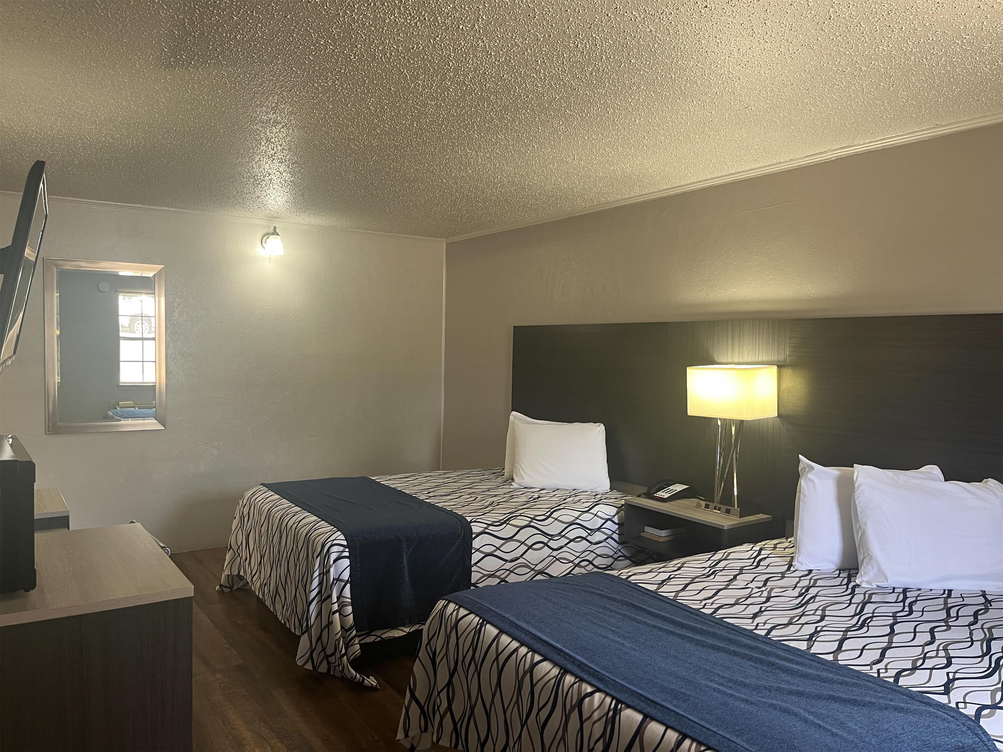 A hotel room with two beds, a desk, a lamp, and a mirror.
