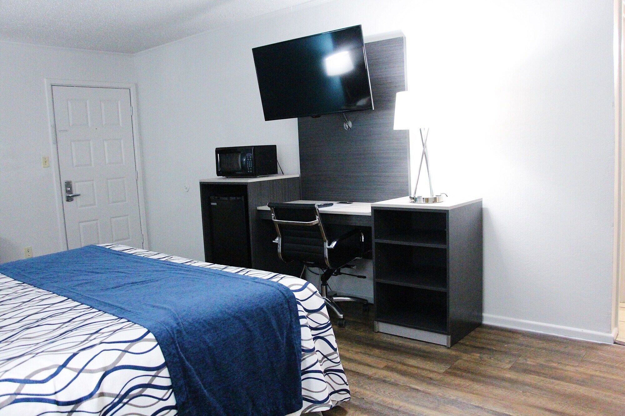 A bedroom with a bed, a desk, a chair, a television, and a microwave.