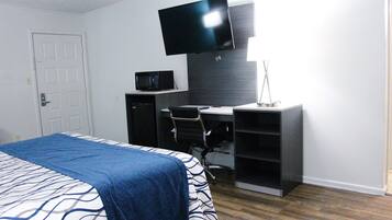 A bedroom with a bed, a desk, a chair, a television, and a microwave.