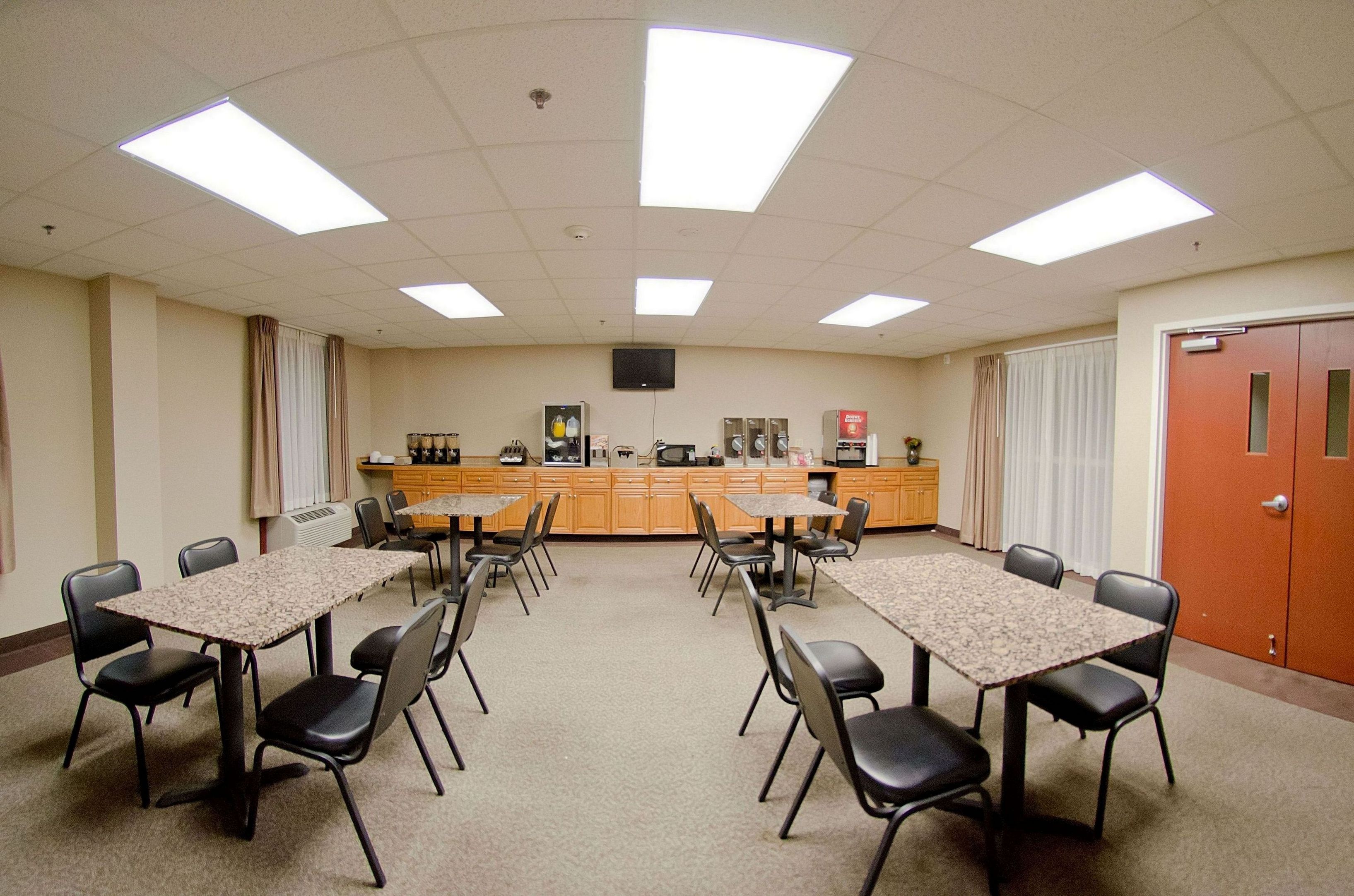 A conference room with a central table, surrounding chairs, a kitchenette, and a door.