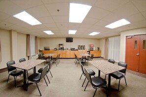 A conference room with a central table, surrounding chairs, a kitchenette, and a door.
