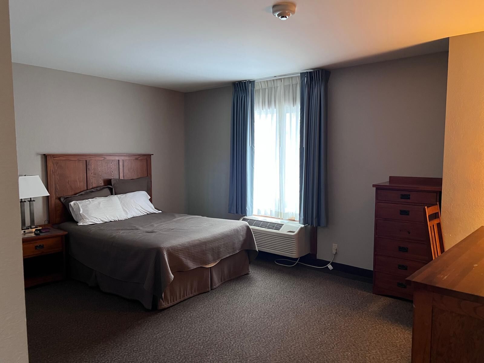 Una habitación de hotel con una cama, una mesita de noche, un aparador y una ventana con cortinas.