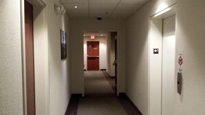A hotel hallway with a carpeted floor, a fire alarm on the right, and a door at the end. - Pleasant Night Inn Carthage Near Fort Drum (Carthage)