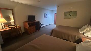 A hotel room with two beds, a desk with a lamp, a television, and a dresser.