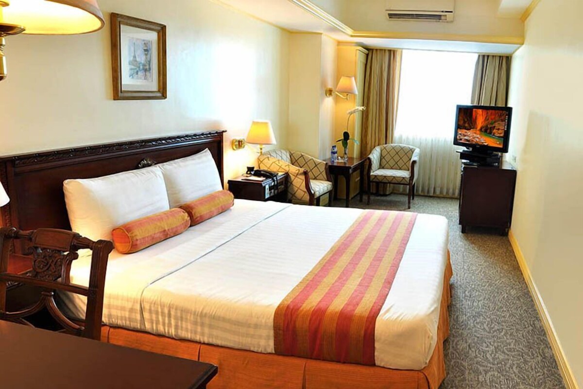 A hotel room with a large bed, a desk, a chair, a television, and a window with curtains.