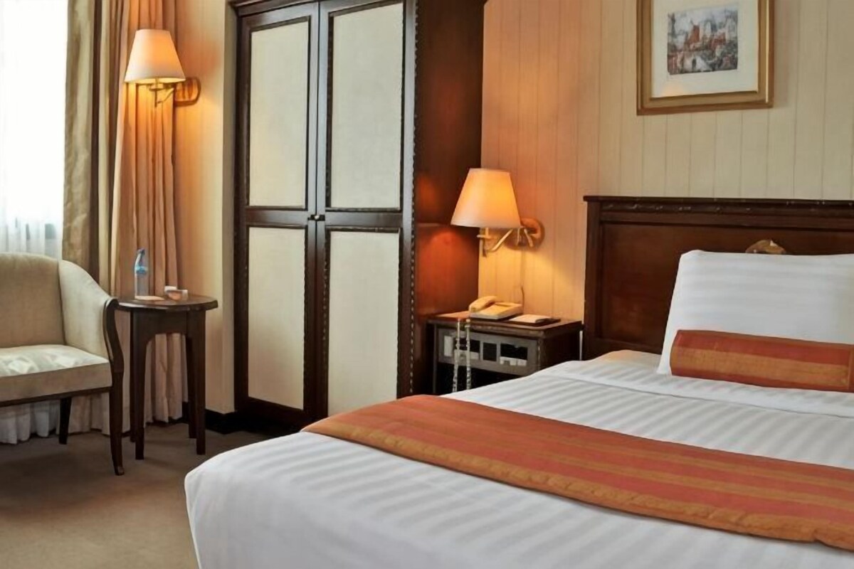 A hotel room with a bed, bedside table, lamp, chair, and a door with a panel design.