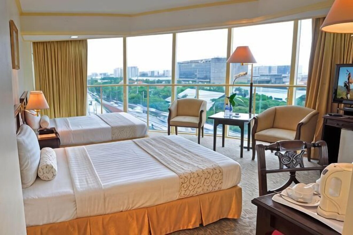 A hotel room with two beds, a desk, a chair, a TV, and a large window with a city view.