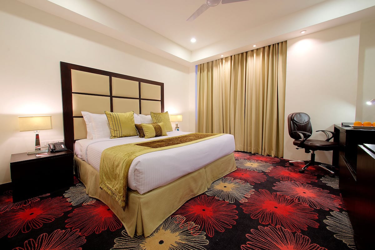 A hotel room with a large bed, a desk, a chair, and a ceiling fan.