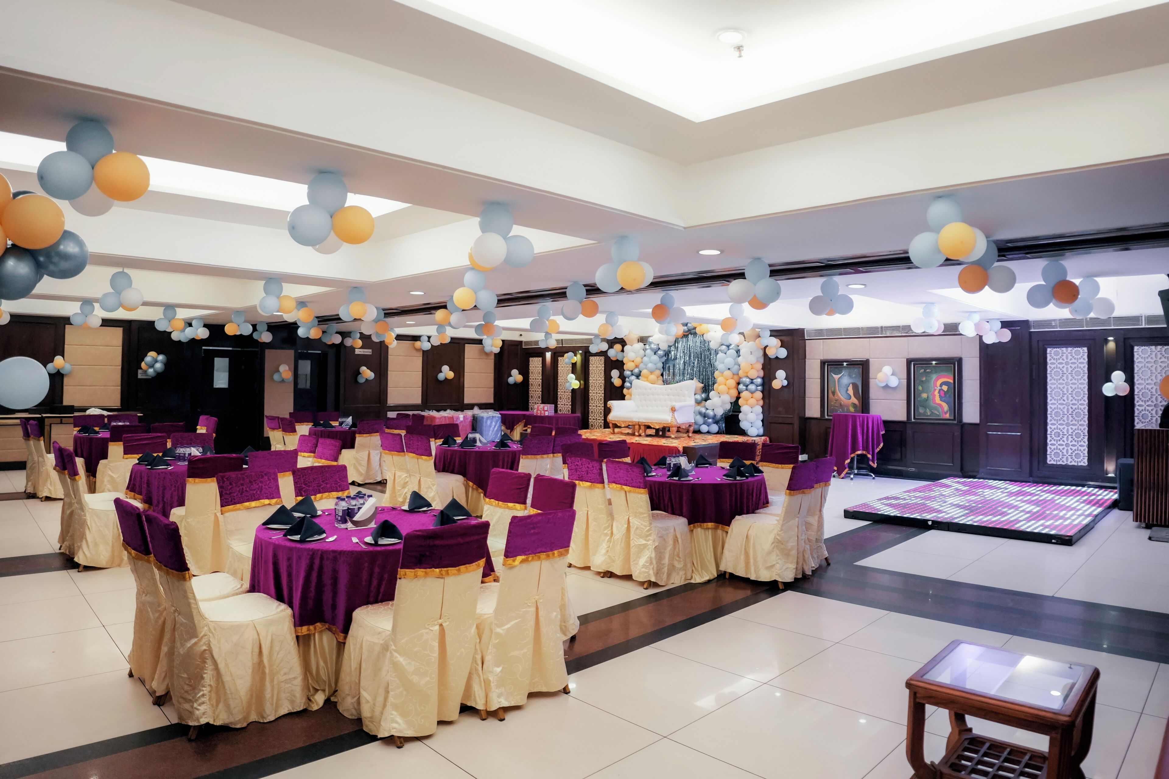 A banquet hall with round tables, chairs, and a stage area.