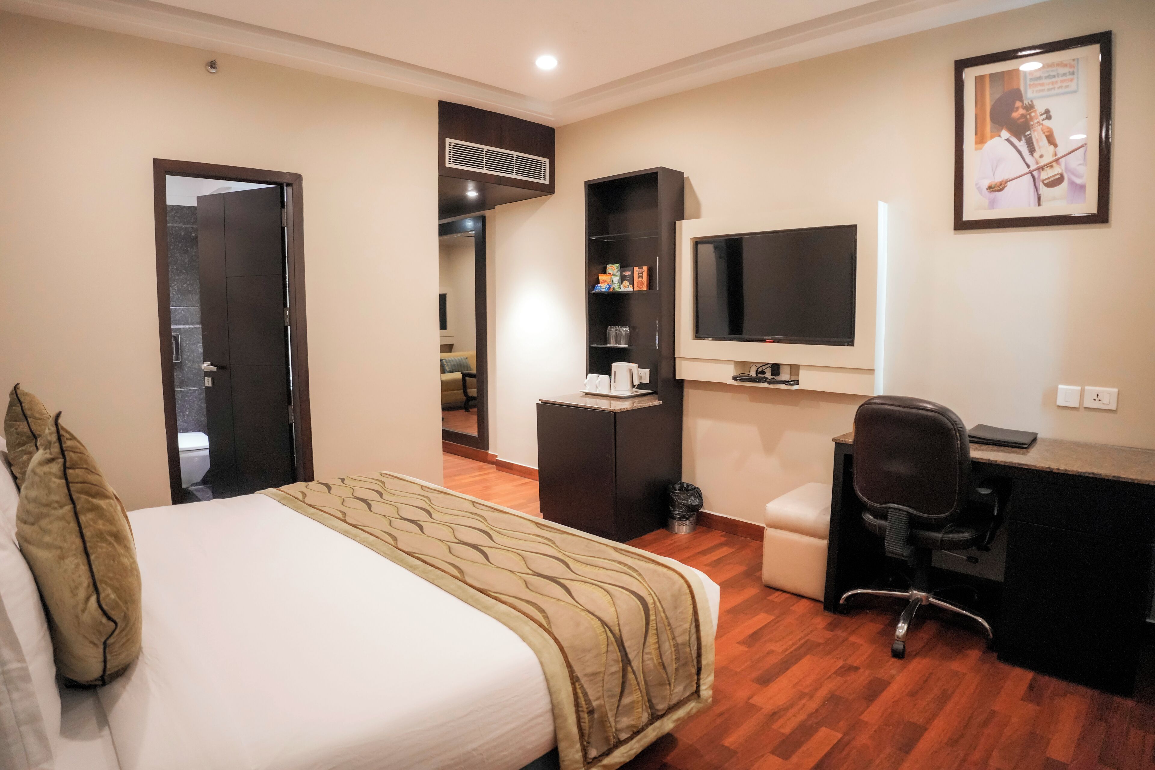 A hotel room with a bed, a desk, a chair, a television, and a small shelf with toiletries.