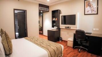 A hotel room with a bed, a desk, a chair, a television, and a small shelf with toiletries.