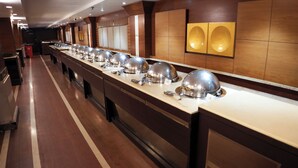 A buffet setup with multiple serving stations, a long counter, and a wooden wall with decorative panels. - Clarion Inn Stella (Bathinda)