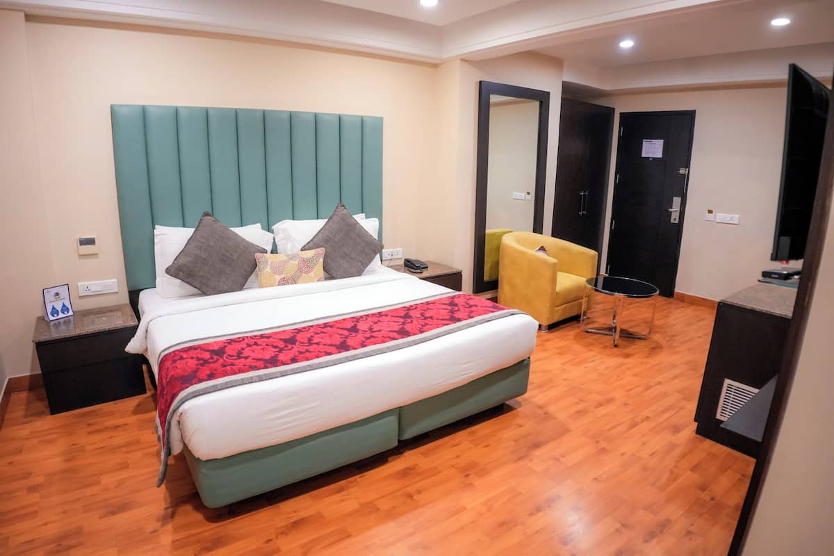 A hotel room with a large bed, a bedside table, a chair, a TV, and a wardrobe.