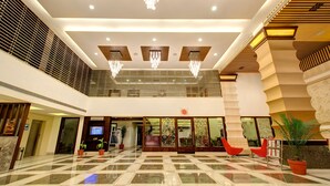 A spacious lobby with a checkered floor, modern chandeliers, and red seating areas. - Clarion Inn Stella (Bathinda)