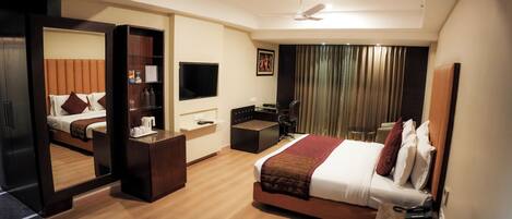 Habitación de hotel con cama, escritorio, silla, televisor y ventilador de techo.
