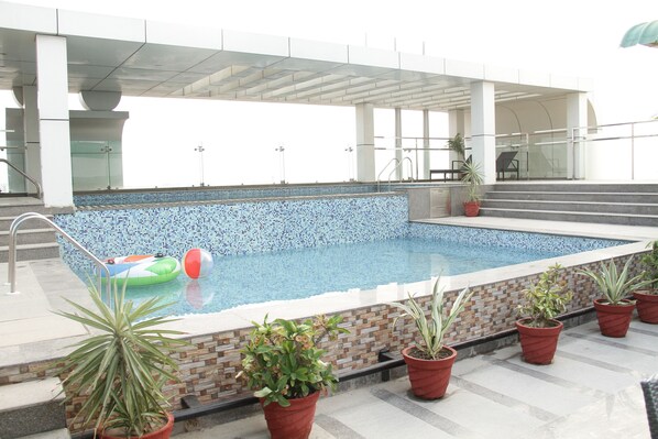 Une piscine dont le bord est revêtu de carreaux, agrémentée de plantes en pot et dotée d’une balustrade en verre.