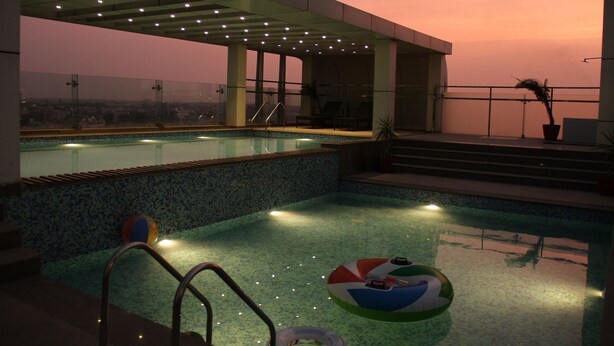 A rooftop pool with a view of the city at sunset, surrounded by glass railings and lounge chairs. - Clarion Inn Stella (Bathinda)