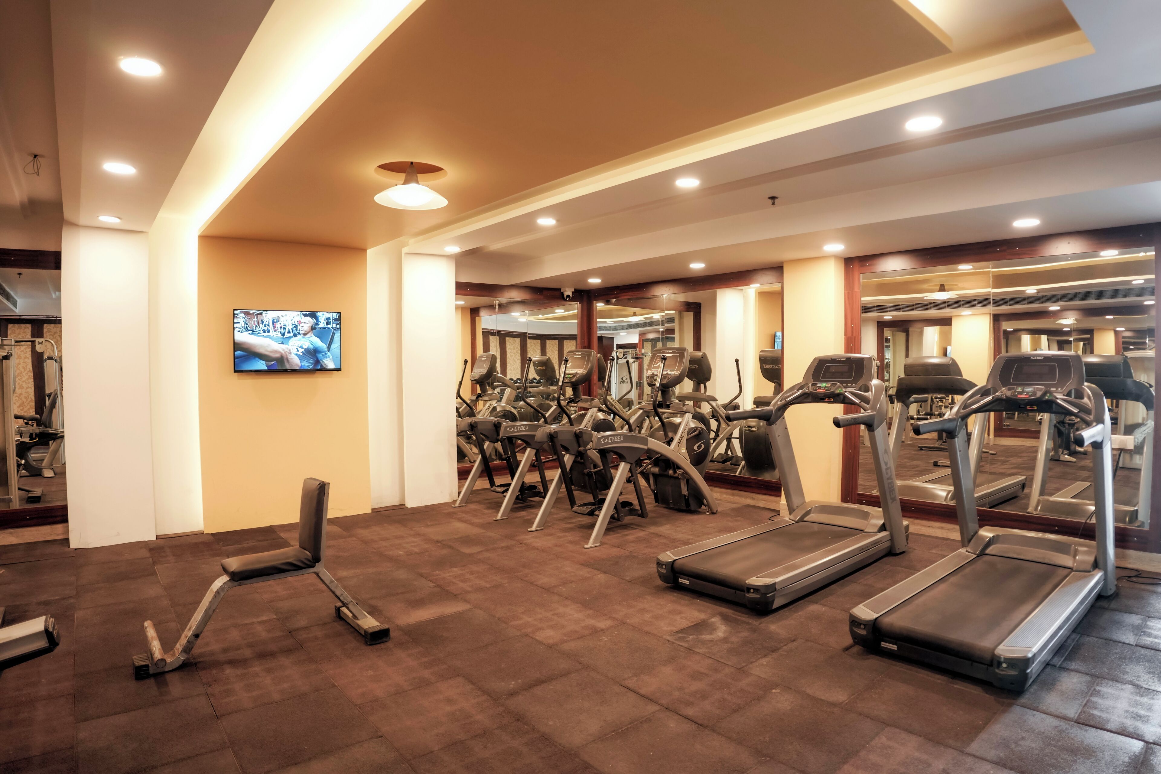A gym with treadmills, elliptical machines, and a television on the wall.