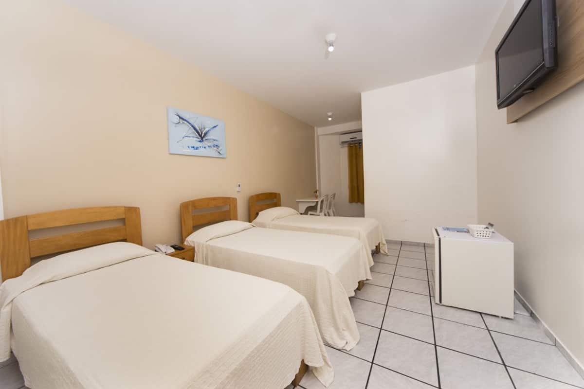 A hotel room with two beds, a television mounted on the wall, a small table, and a washing machine.