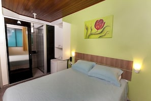 Quarto com cama, um quadro na parede e banheiro visível por uma porta aberta.