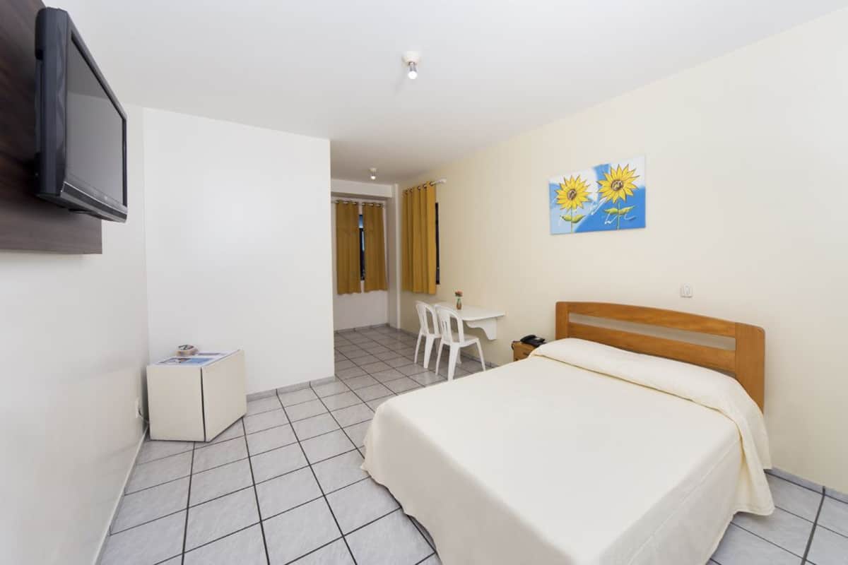 A hotel room with a bed, a desk, a chair, a television, and a painting on the wall.