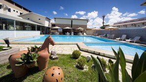 Una piscina amb gandules i ombrelles, envoltada d'un edifici amb teulada emblerta i cel serè.