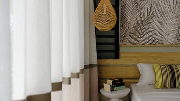 A bedroom with a bed, a bedside table with books, a hanging wicker lamp, and a wall with a leaf pattern.