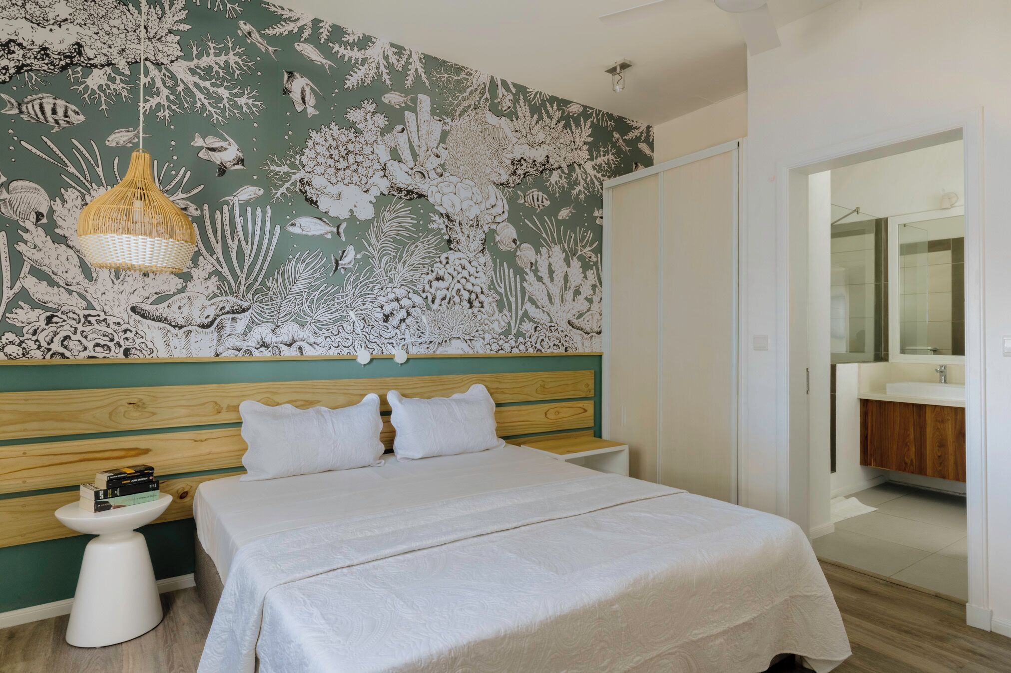 Un dormitorio con cama, mesitas de noche, un mural en la pared y un baño visible a través de una puerta abierta.