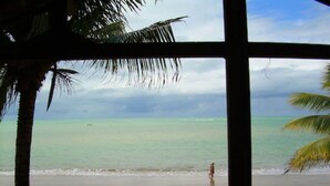 Uitzicht op een strand door een raam, met palmbomen, een zandstrand en de oceaan.