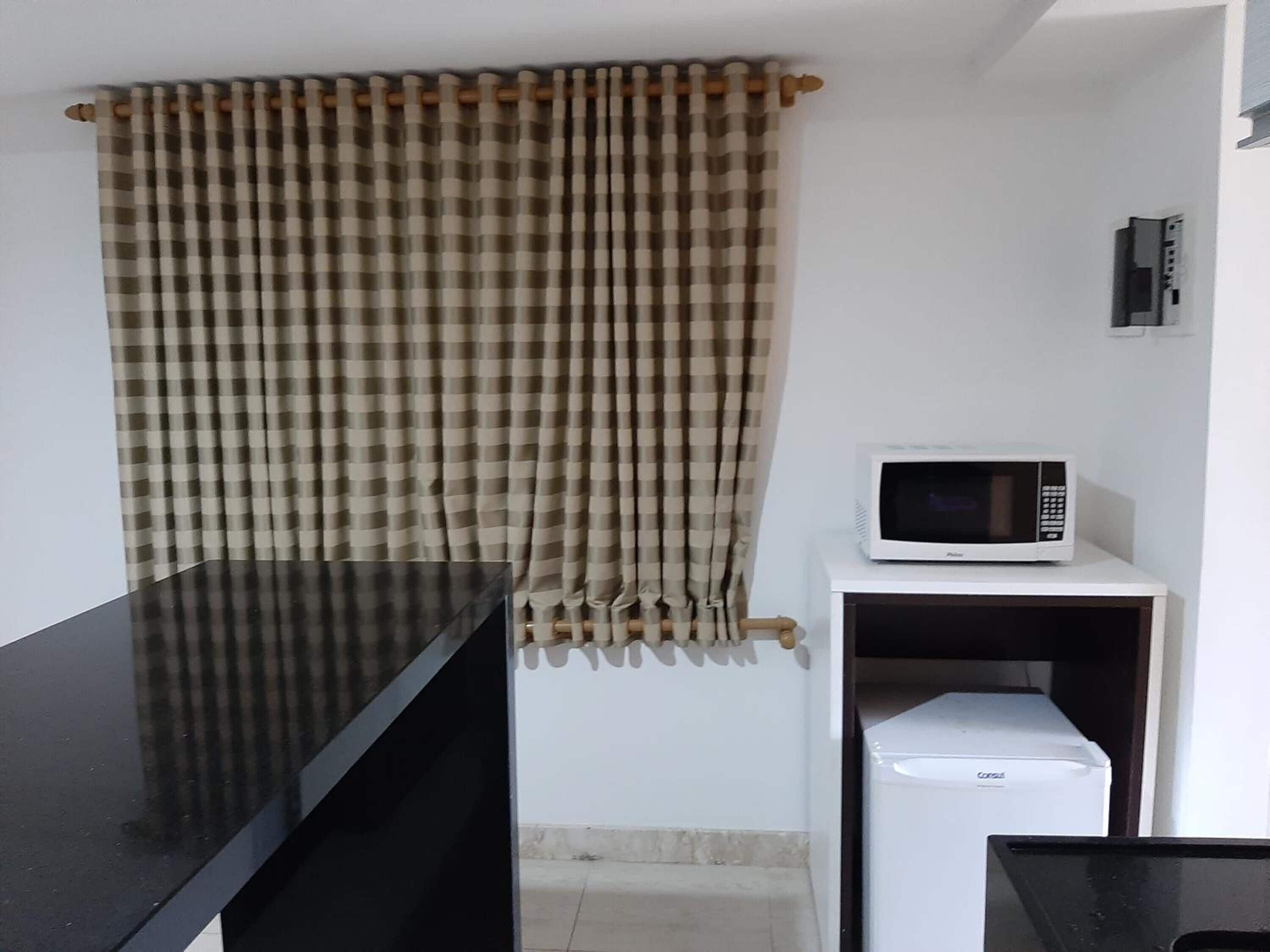 A kitchen with a black countertop, a microwave on a white shelf, and a checkered curtain.