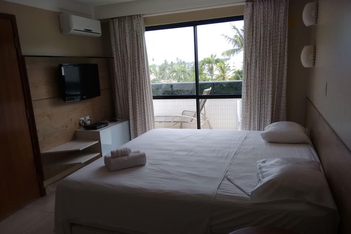 Une chambre d’hôtel comprenant un lit, un téléviseur fixé au mur, un bureau avec une chaise et une fenêtre avec des rideaux.