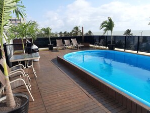 Un área de piscina en la azotea con sillones de descanso, una mesa y plantas en macetas.